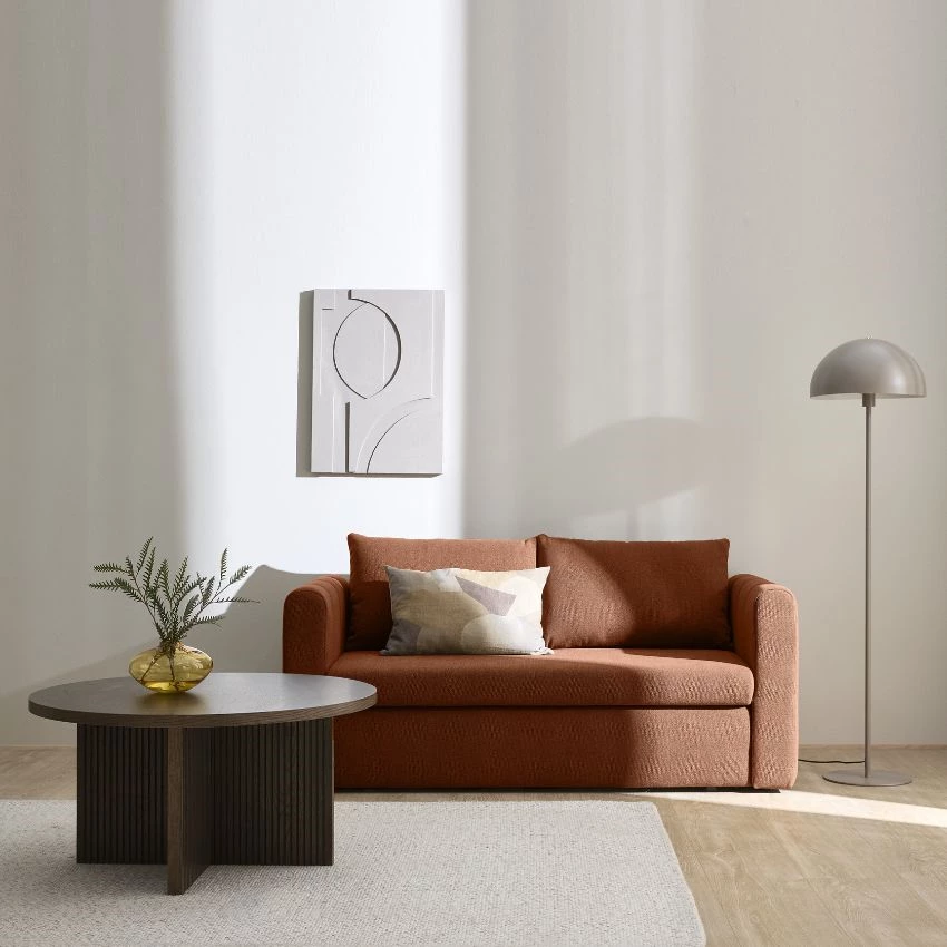 Rød sovesofa i stuemiljø med sofabord, gulvlampe og tæppe